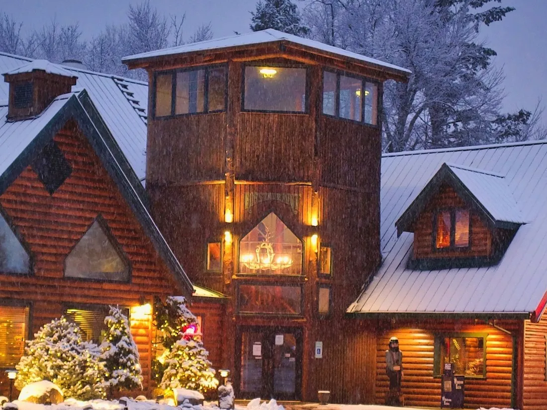 Sumas Mountain Lodge on a snowy evening, its log gables and tower glowing with warm light